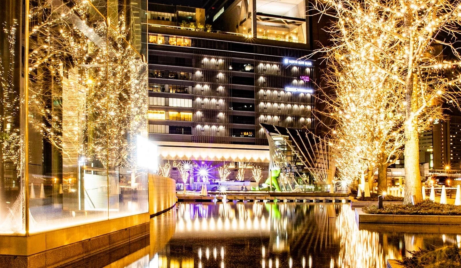 夜晚的 Grand Front Osaka 梅北廣場被香檳金燈光包圍,街樹與建築倒映在水池中,光影璀璨