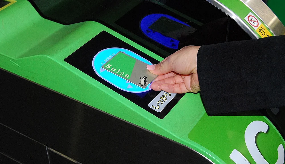 一隻手將 Suica 卡放在綠色自動剪票機的感應區上,閘門亮起藍色燈光示意可通行