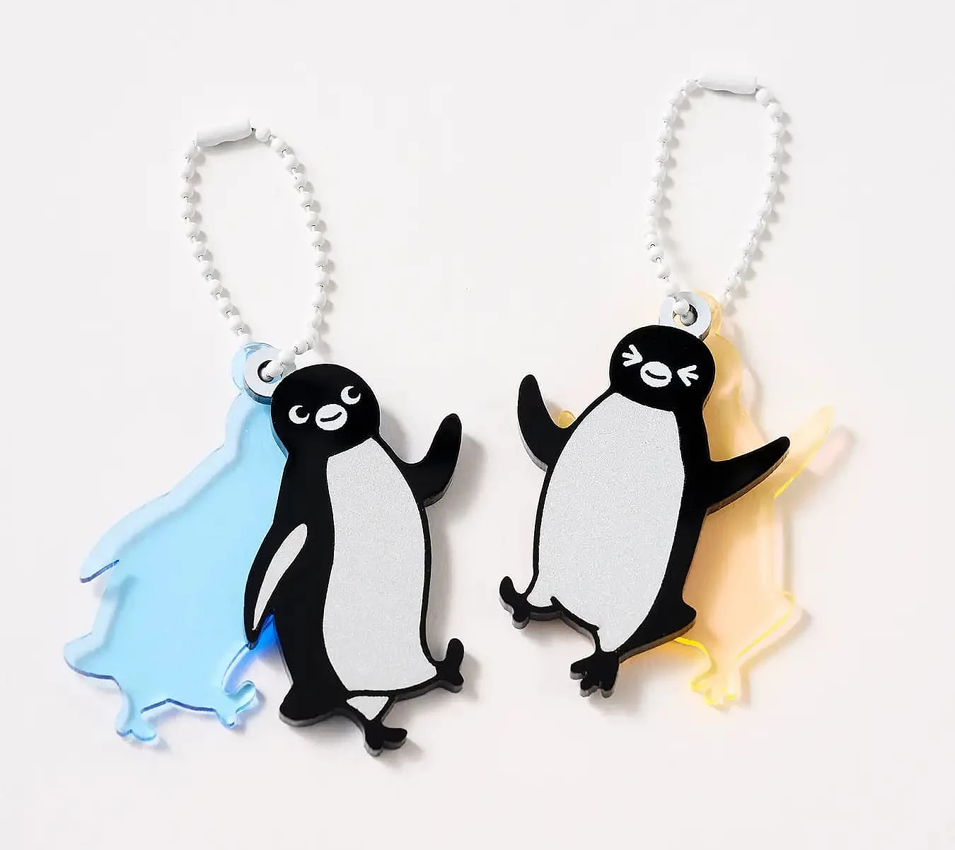 兩個「Suica 企鵝」壓克力鑰匙圈,一個搭配藍色透明背板、另一個搭配黃色背板,皆呈現小企鵝側身揮手的造型,附白色珠鍊