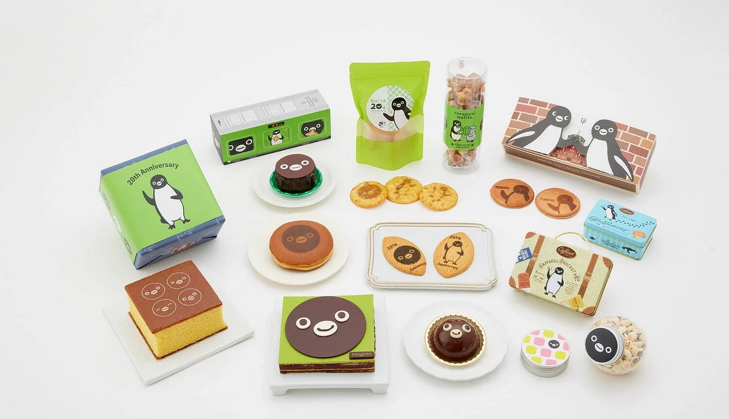 一組以 Suica 企鵝為主題的甜點與零食組合,擺放有蛋糕、銅鑼燒、餅乾、鐵盒糖果與盒裝點心等,每款包裝上都印有 Suica 企鵝插畫