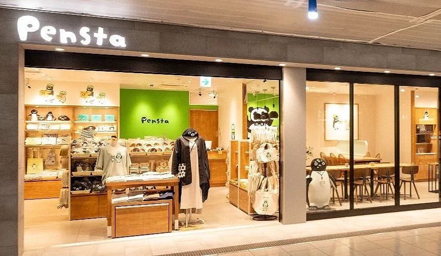 Pensta 店面的外觀照片,明亮的玻璃櫥窗展示多款 Suica 企鵝商品,店內以綠色與木質裝潢為主調,入口處可見服飾與周邊陳列