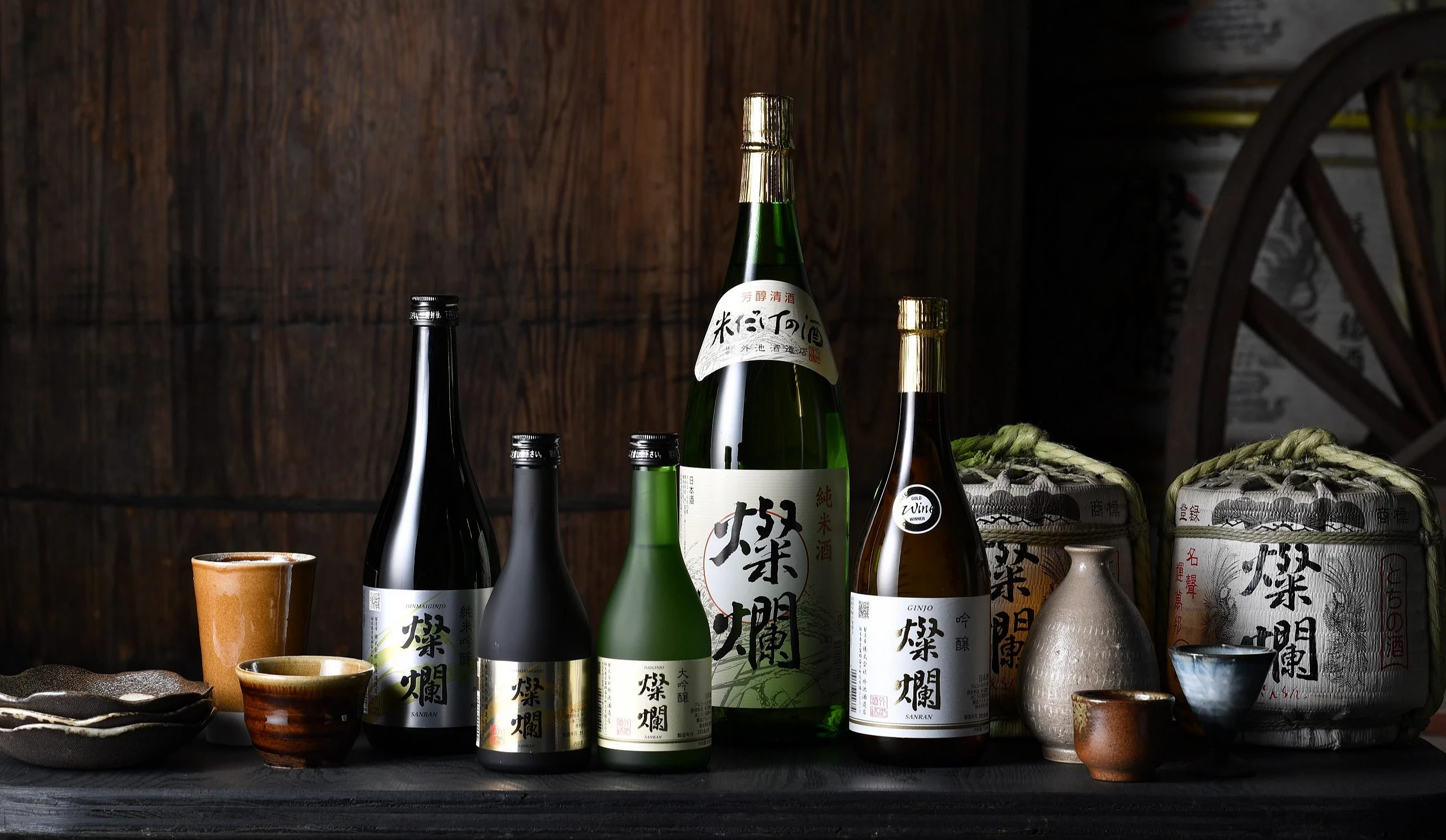 多款栃木縣日本酒陳列於木桌上,包含外池酒造店的「燦爛」系列酒瓶與酒器