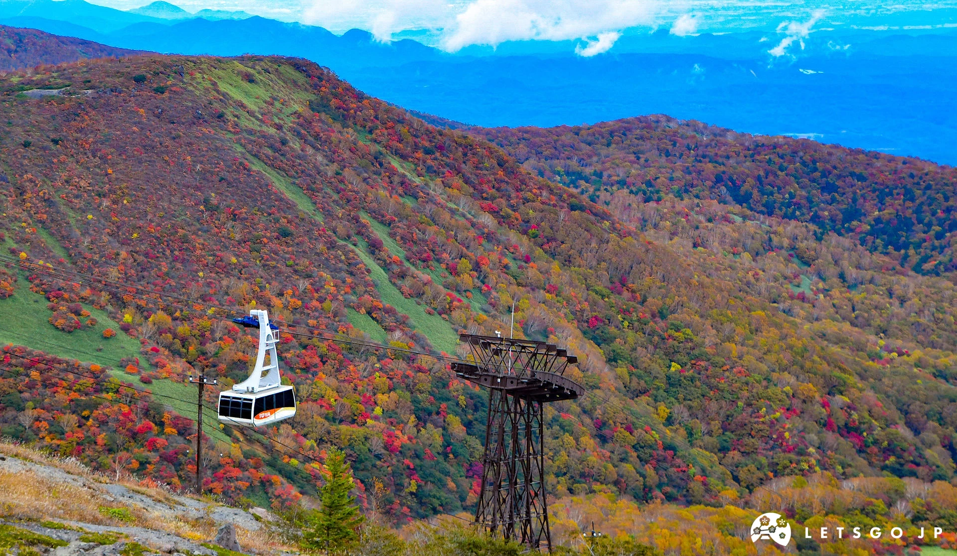 秋季那須高原山區,纜車行駛在染紅的山林上方,遠方可見層層紅黃交錯的楓葉山巒景色