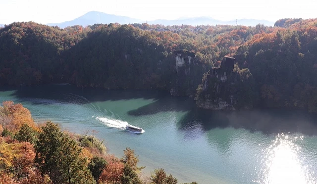 惠那峽湖面景色,遊船行駛在被岩壁與森林環繞的水道上,岸邊樹木呈現秋季紅黃相間的色彩