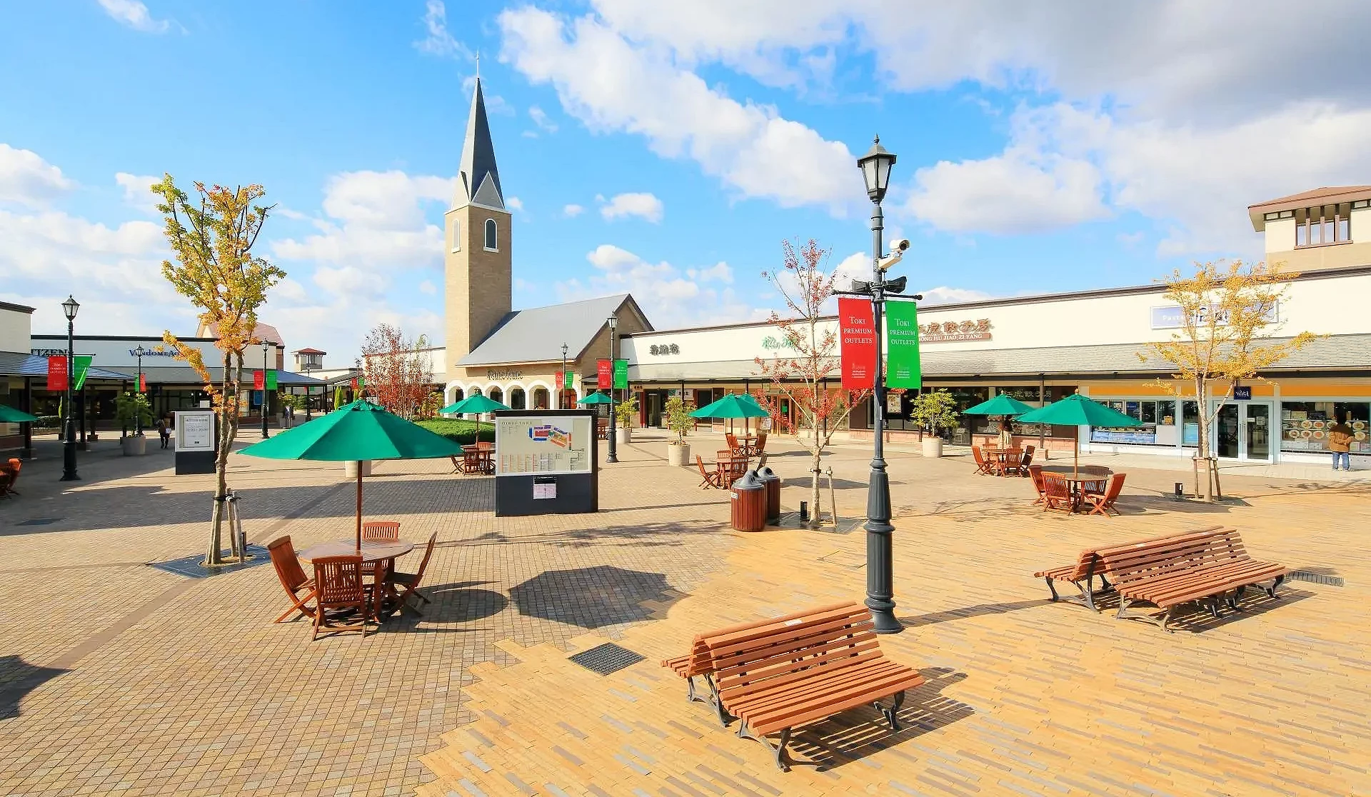 土岐 Premium Outlets 園區的中庭景色,木製座椅、綠色陽傘與歐式鐘塔在晴空下