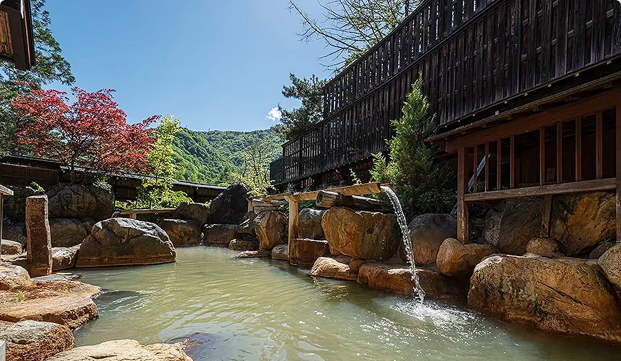 露天溫泉以大量岩石與木製湯口打造,泉水注入池中,四周可見青山與樹木,景色明亮而放鬆