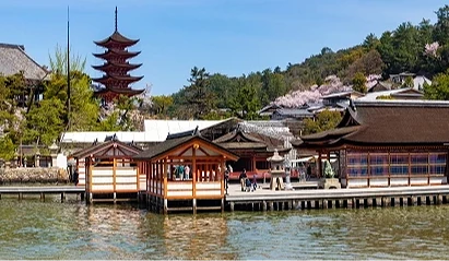 嚴島神社社殿與海上迴廊,朱紅建築映照海面,後方可見五重塔與山林景色