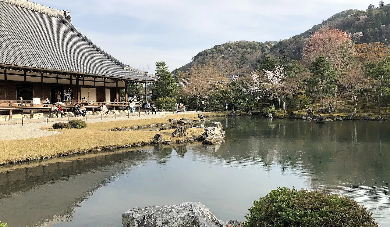 庭園水池旁有著四面建築與群山樹木和少許櫻花