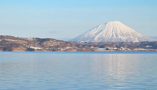 冬季洞爺湖湖景,平靜湖面倒映藍天,遠方可見覆雪的羊蹄山,近景有數隻野鴨在湖上游動