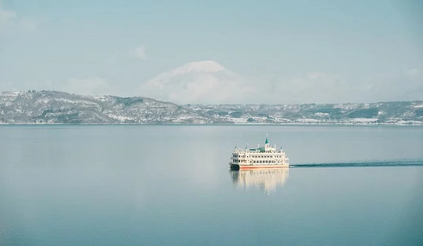 洞爺湖遊覽船航行於湖面中央,背景為雪景山巒與開闊湖景,呈現北海道洞爺湖的湖上巡航景色