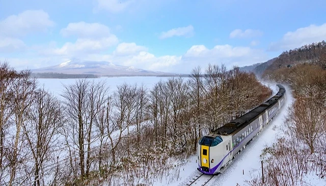 冬季北海道列車行駛於洞爺湖附近,鐵道兩側覆雪,遠方可見結冰湖面與冬日山景