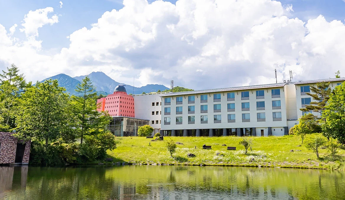清里高原度假飯店外觀,建築座落於森林與湖畔之間,背景可見八岳山景,呈現北杜市高原地區清新寧靜的住宿氛圍