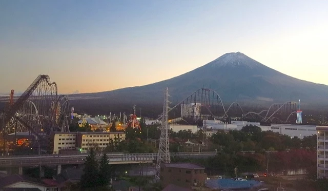 傍晚時分遠望富士急樂園與富士山景色,遊樂設施剪影在夕陽下清晰可見,呈現富士山站周邊結合樂園與自然的景觀畫