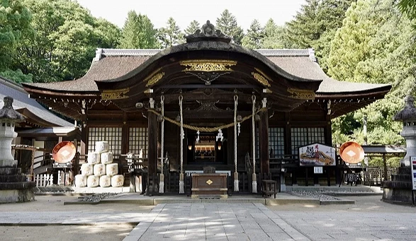 甲府市武田神社本殿景觀,傳統木造神社建築坐落於林間,前方可見參道與奉納酒樽