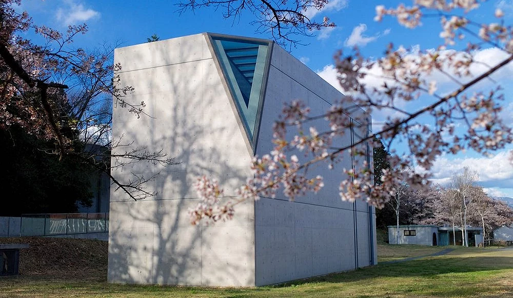 小淵澤光之美術館現代建築外觀,清水混凝土建築佇立於草地間,前景櫻花點綴