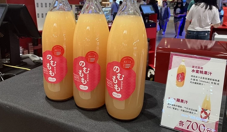 三瓶福島產桃子原汁(のむもも)的近照,瓶身標籤呈現亮粉色,液體呈天然的乳黃色。