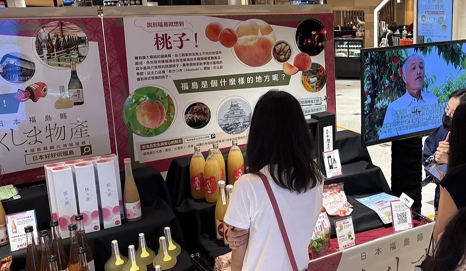 展位遠景,民眾在「POP UP STAGE」櫃台前諮詢,電視螢幕正播放福島當地的宣傳影片。