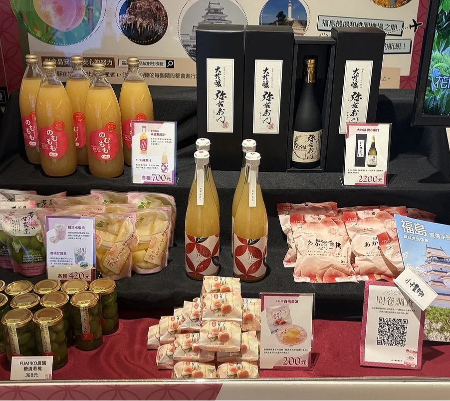 展櫃特寫,陳列著福島產的桃子果汁瓶、數盒桃子口味點心以及後方包裝精緻的清酒禮盒。