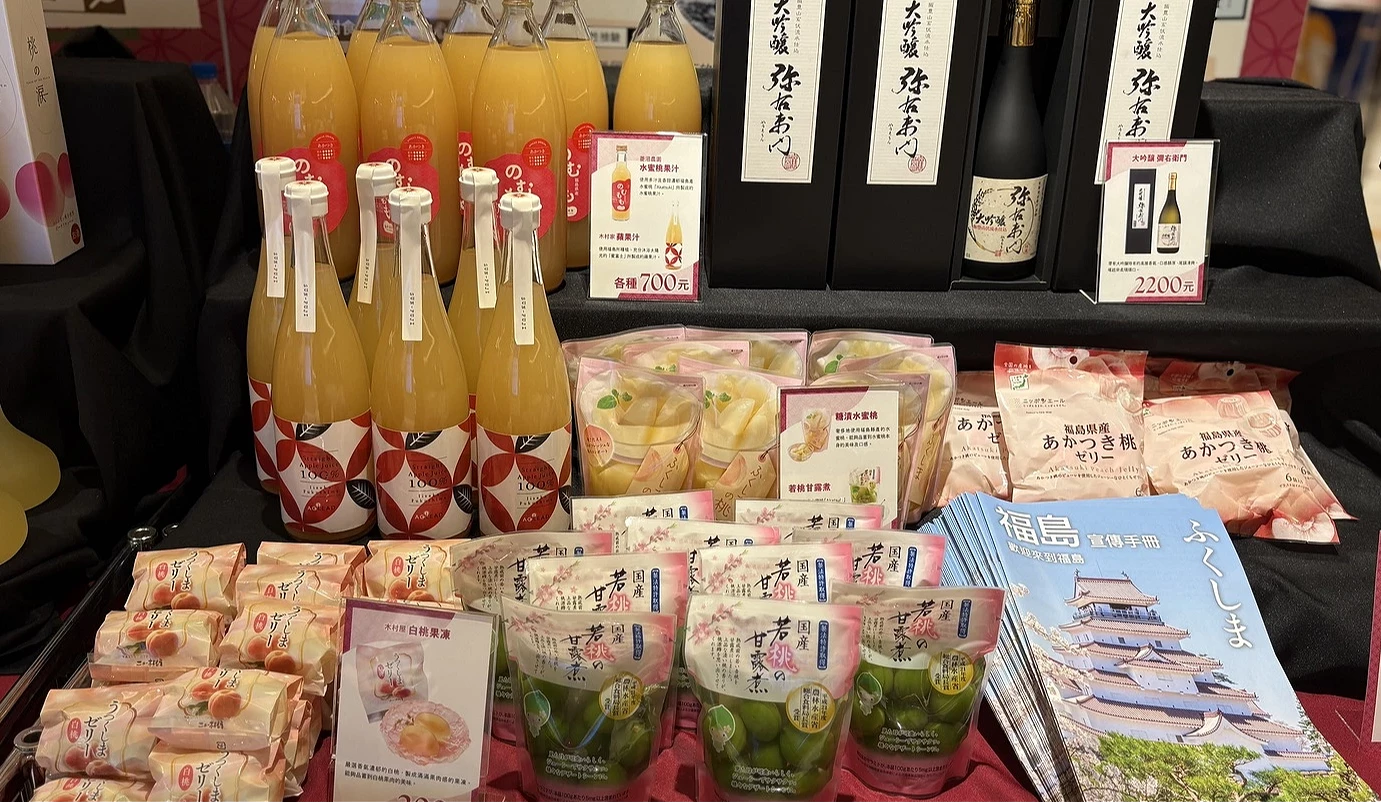 商品陳列近照,包含整排的桃子果汁、日本清酒,以及精美包裝的福島觀光導覽手冊與點心。