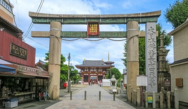 大阪四天王寺著名的石鳥居正面觀,石製鳥居上方懸掛著金色文字的匾額,穿過鳥居可看見遠方的西門(極樂門)與五重塔,石柱旁立有「大日本佛法最初四天王寺」石碑