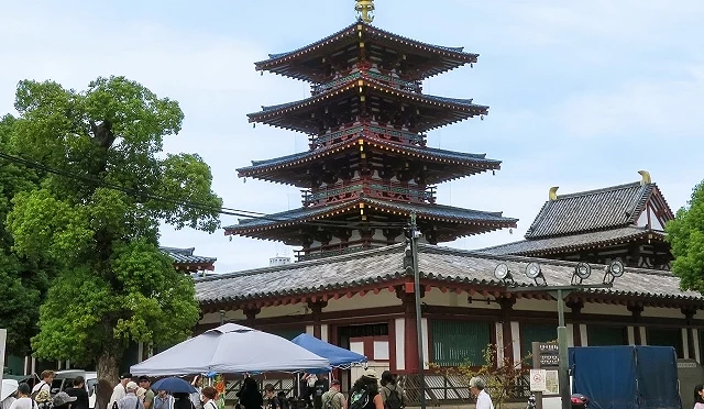 眾多遊客在五重塔與金堂旁的露天攤位前駐足挑選,現場設有藍色與銀色遮陽帳棚