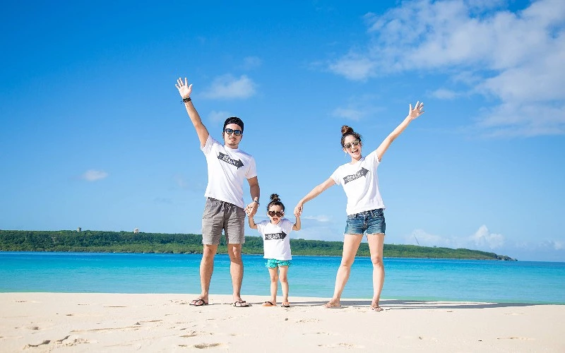 沙灘上一家三口牽手站立,三人穿著印有 BEACH 字樣白色上衣