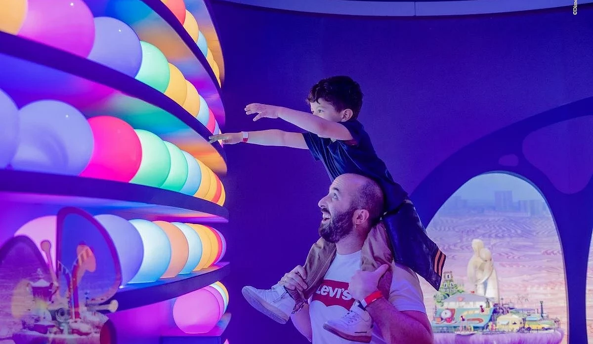大人肩上背著小孩,小孩正在摸彩色發光的球體