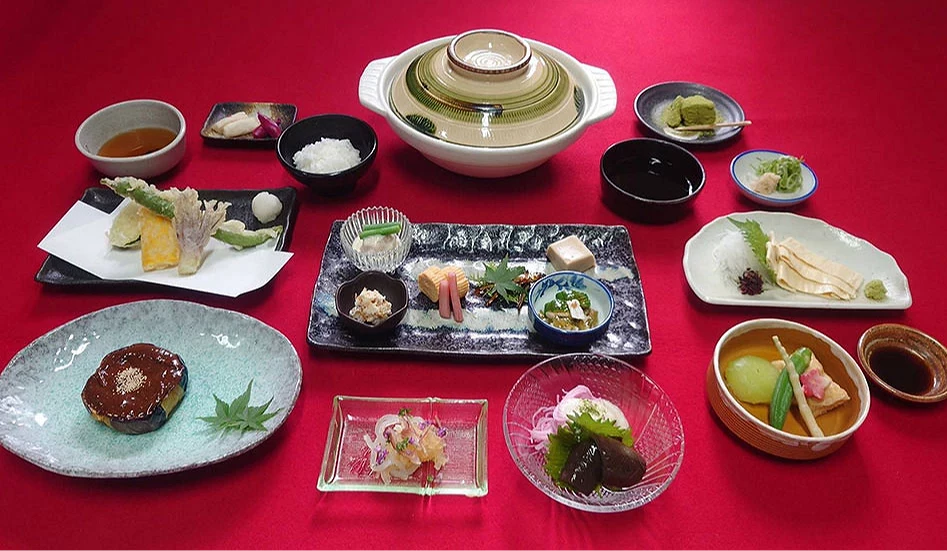 嵐山精進料理套餐擺盤示意,多道以豆腐、湯葉與當季蔬菜製作的料理整齊排列於紅色桌布上,包含湯豆腐、天婦羅、小鉢與米飯