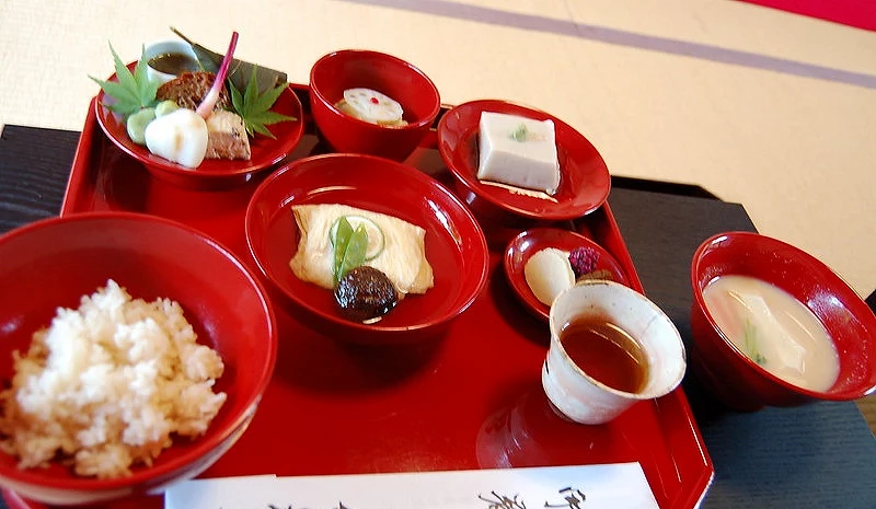 天龍寺境內精進料理「篩月」的套餐擺盤,紅色漆器托盤上盛放白飯、湯品、豆腐與湯葉料理,以及多道以當季蔬菜製作的小鉢