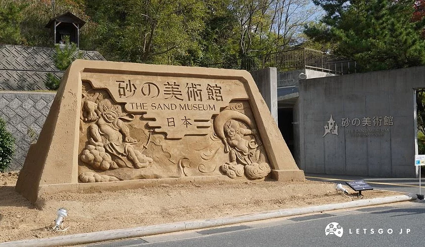 鳥取砂之美術館入口沙雕招牌,上方刻有「砂の美術館 THE SAND MUSEUM」字樣,展示精緻立體沙雕藝術