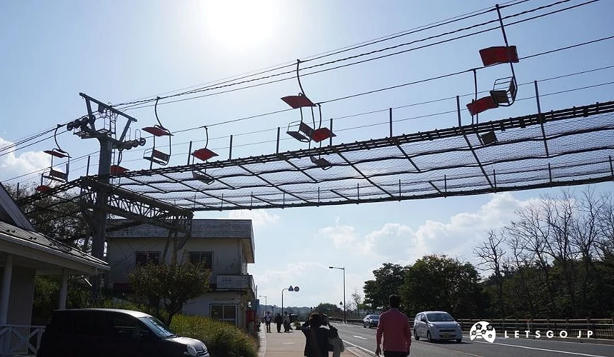 鳥取砂丘觀光纜車在道路上方運行,紅色座椅懸掛於半空,遊客於下方步行與車輛通行