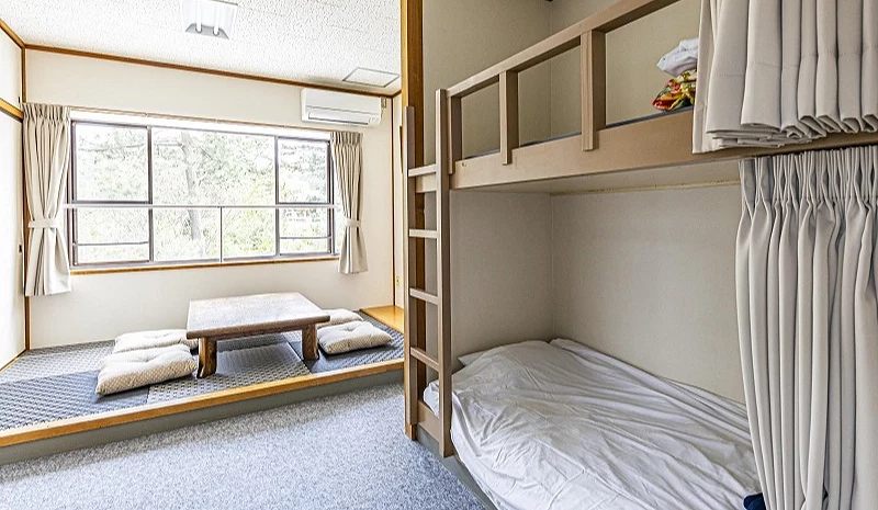 鳥取住宿客房內部,設有上下舖床位與榻榻米小桌區,窗外可見綠意景色