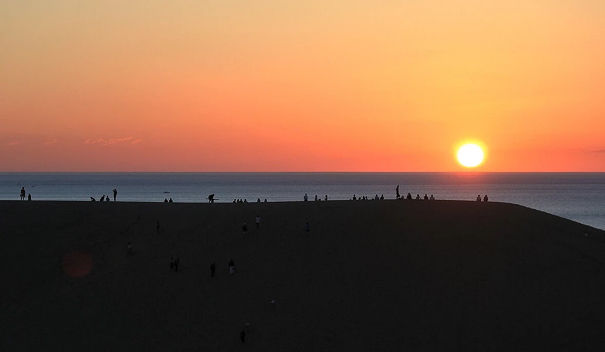 鳥取砂丘夕陽景色,太陽緩緩沉入日本海,遊客剪影佇立沙丘上欣賞日落