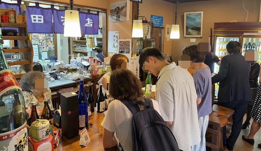 外國旅人與當地居民在小倉酒舖內並肩站立品飲,融入日本日常的角打社交體驗