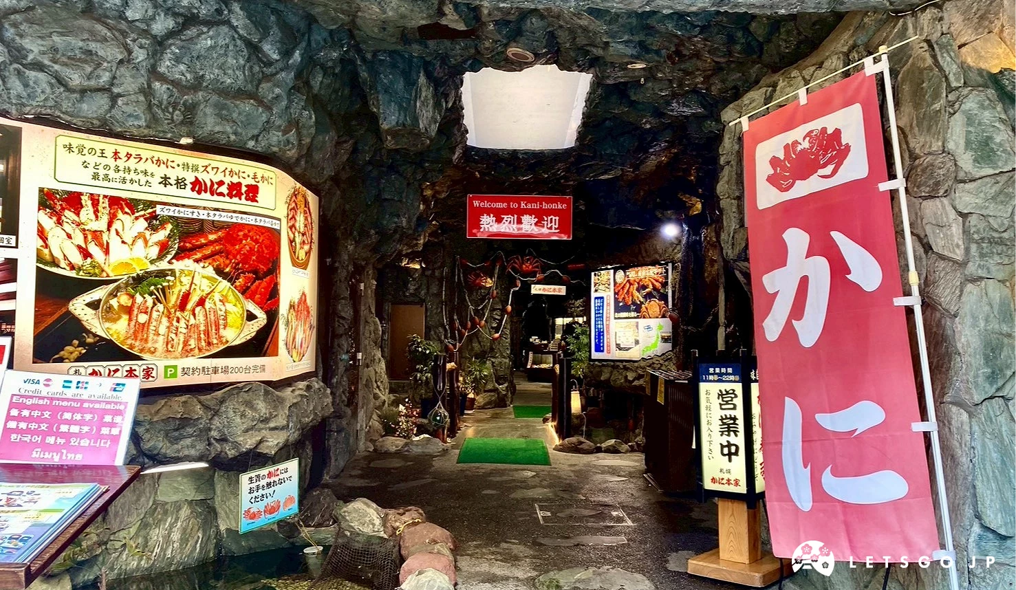 札幌螃蟹本家仙台店的入口實景,石牆結構搭配日式紅色布簾與菜單告示牌,呈現獨特的洞窟風格走廊。