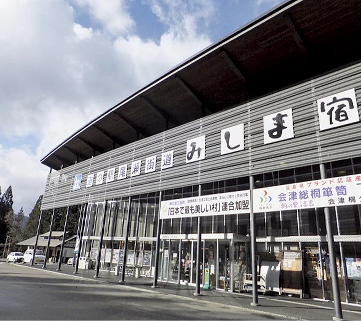 日式建築風格的駅舍停靠站,白色波浪鐵皮牆面標註日文站名,停車場前方停放數台車輛。