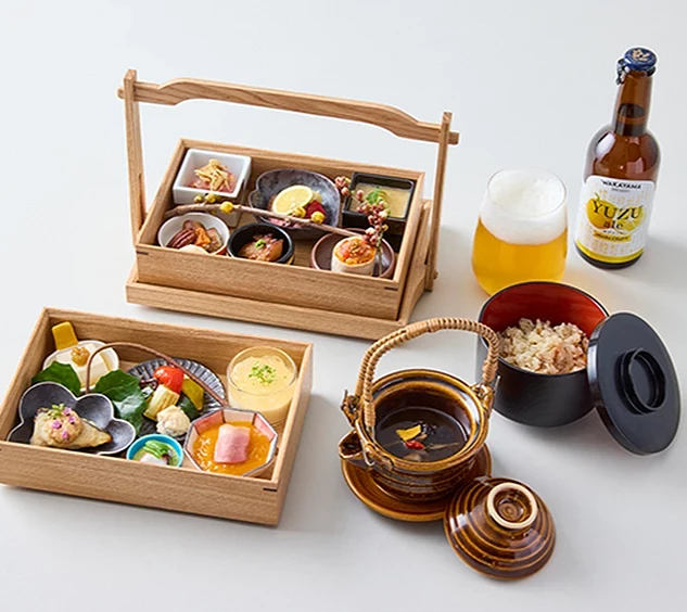 木質餐盒裡放了各式精緻料理,旁邊有碗裝料理、湯品、啤酒