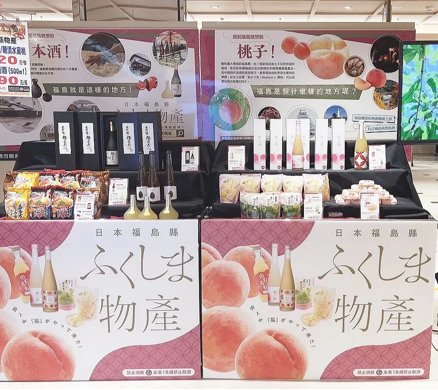 福島物產展的展位佈置,背景牆印有大顆水蜜桃圖案,架上陳列著多瓶桃子果汁與相關禮盒。