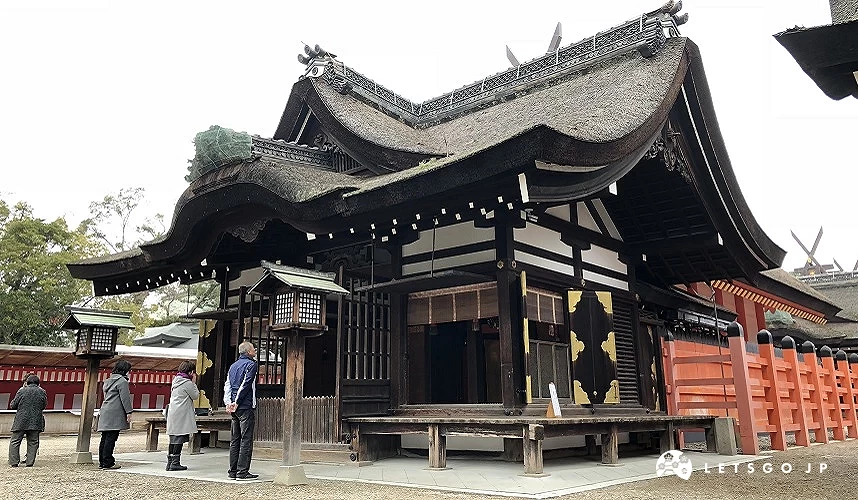 住吉大社本殿建築外觀,茅草屋頂與住吉造樣式明顯,參拜者站立於殿前