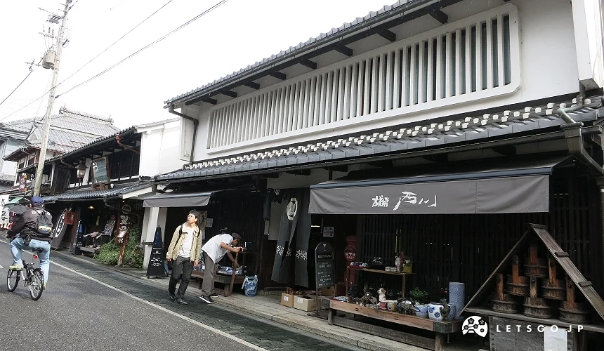 傳統商家街道,白壁黑格子建築,店招寫有「蔵 西川」,行人與腳踏車往來
