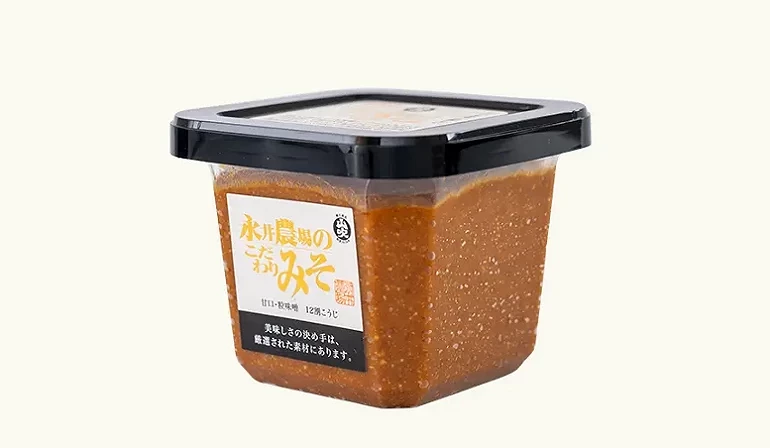 永井農場特製味噌(永井農場のこだわりみそ)的方形透明盒裝外觀,內容物為深棕色的信州味噌,搭配黑色蓋子與白底金黃色字體的標籤