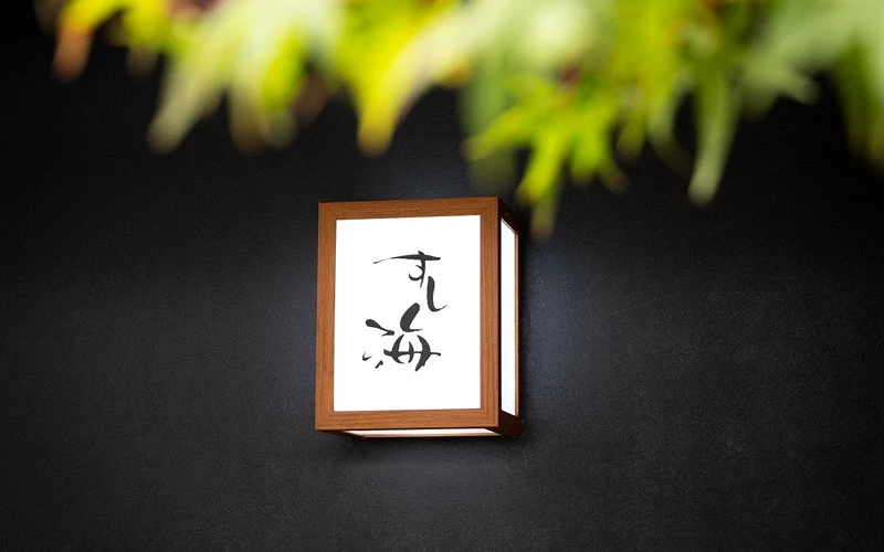 黑牆壁燈上寫有日文標語前景有綠葉