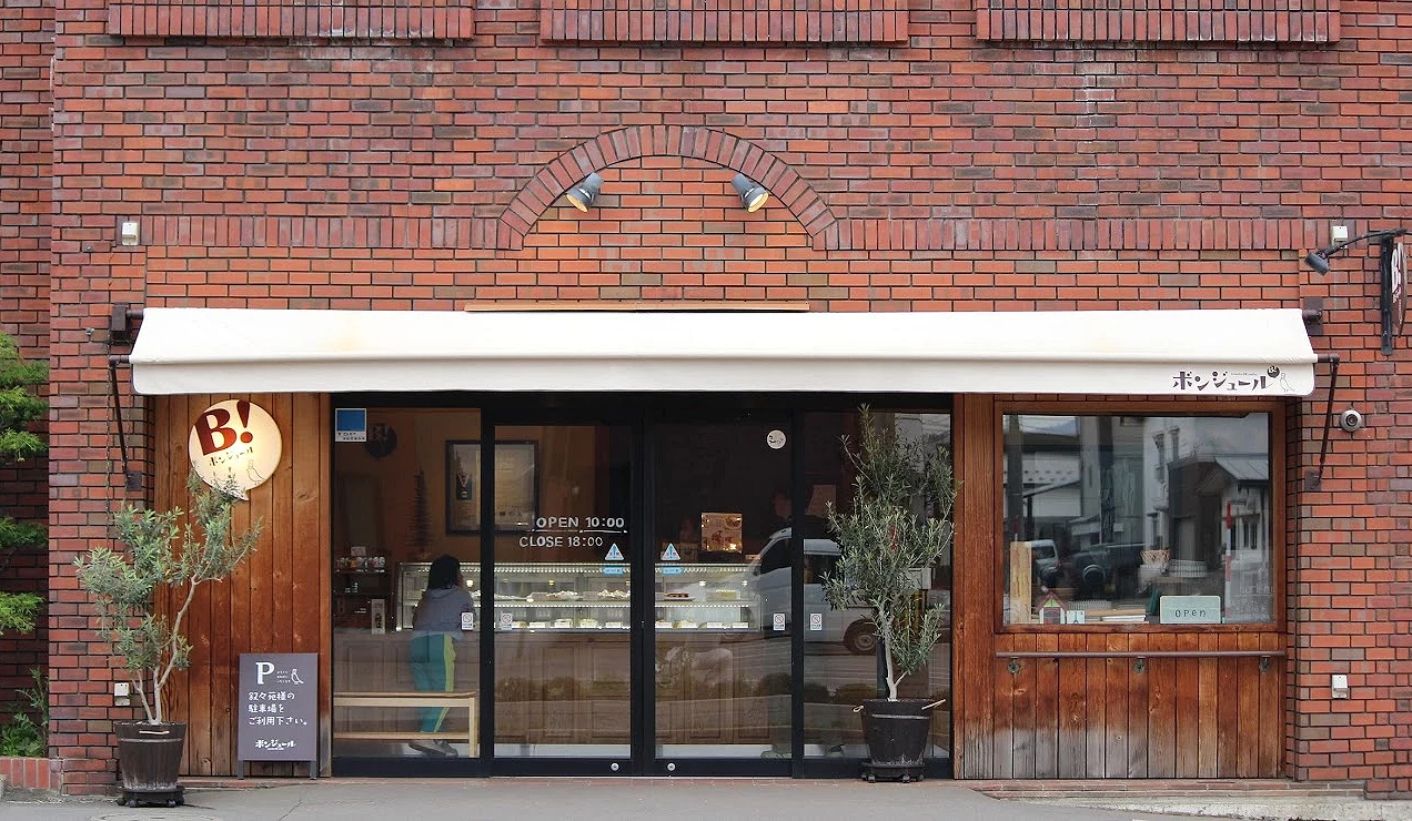 紅磚外牆的ボンジュール甜點店門口,設有玻璃櫥窗與招牌