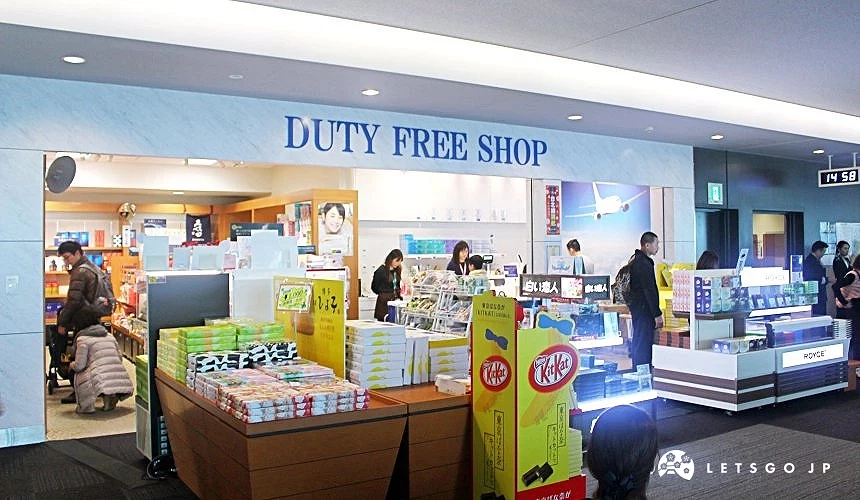 北九州機場國際線候機區內的免稅店,入口標示DUTY FREE SHOP,店內陳列零食、伴手禮與美妝商品,旅客正在選購