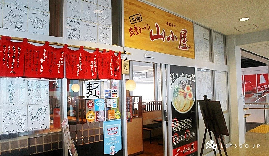北九州機場內的山小屋拉麵店入口,掛有紅色布簾與日式招牌,門口展示拉麵菜單與招牌照片