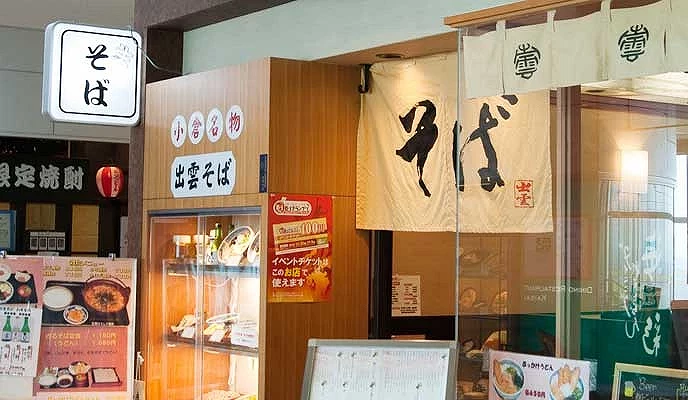 北九州機場內的出雲そば餐廳入口,掛有日式布簾與招牌,門口展示餐點模型與菜單
