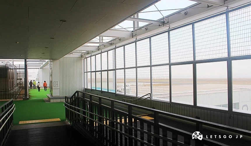 北九州機場室內展望台通道,大片玻璃窗可遠眺機場跑道與海面景色,旅客在走道上散步