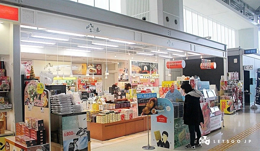 北九州機場內販售在地名產的商店,展示明太子、點心與特色伴手禮,旅客正在選購商品