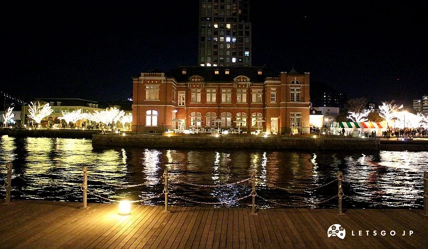 門司港夜景,紅磚建築與燈光倒映於水面,前方為木棧道與欄杆