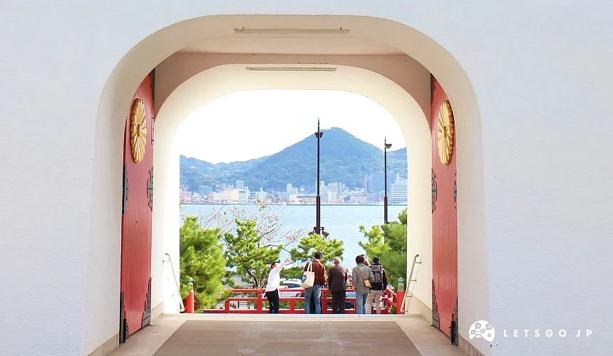 從赤間神宮門內向外望去,框景呈現關門海峽與對岸山景,遊客站在欄杆前眺望